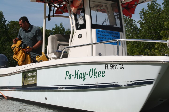 Man on a boat named Pa-Hay-Okee holding yellow life jackets, with Everglades National Park sign visible.
