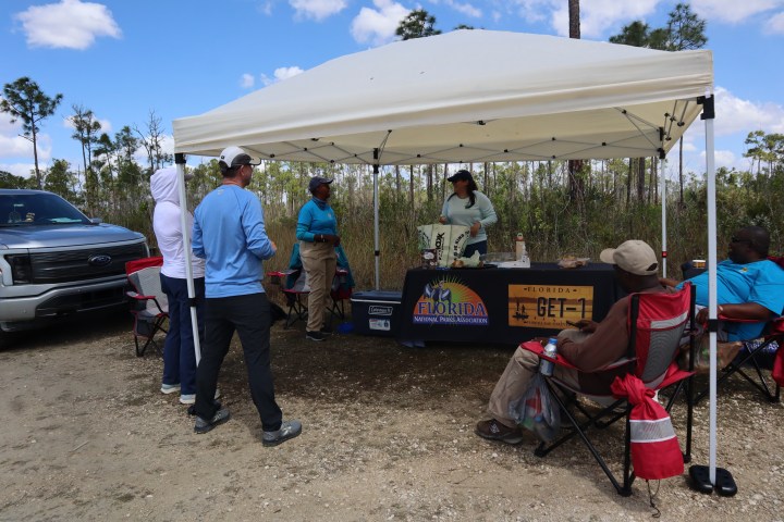 People at an outdoor booth with a canopy, table, and chairs.
