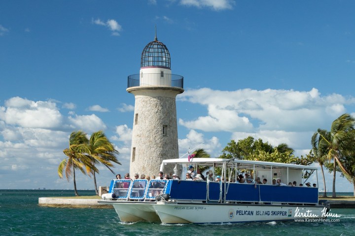 Tour boat near a lighthouse and palm trees on a sunny day.